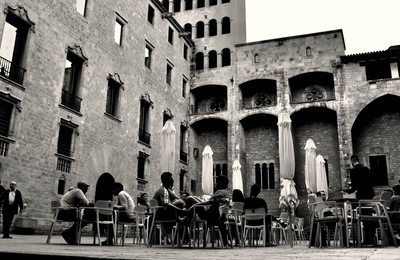 Tables and parasols under the Gothic stone of Plaça del Rei